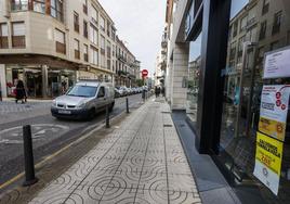 Un coche circula por la calle Joaquín Hoyos frente a un escaparate con carteles contra la ZBE.