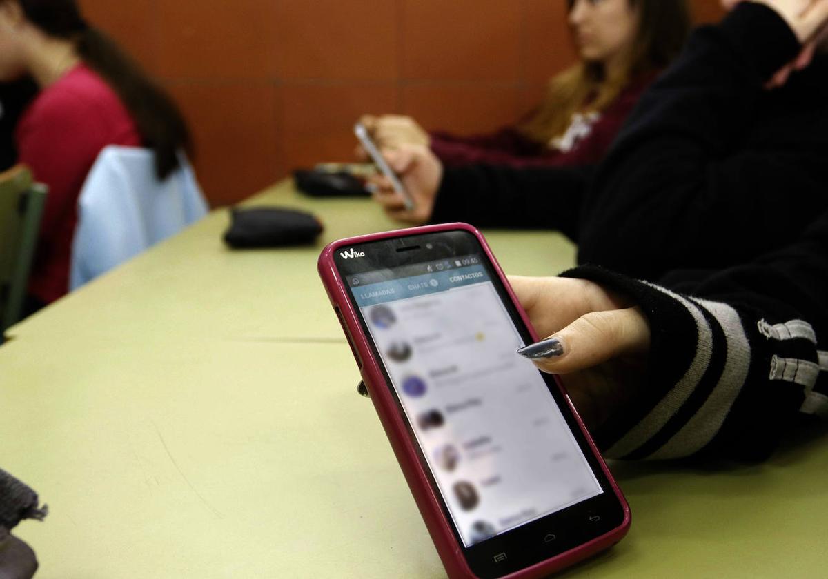 Una adolescente sostiene un teléfono móvil en el aula.