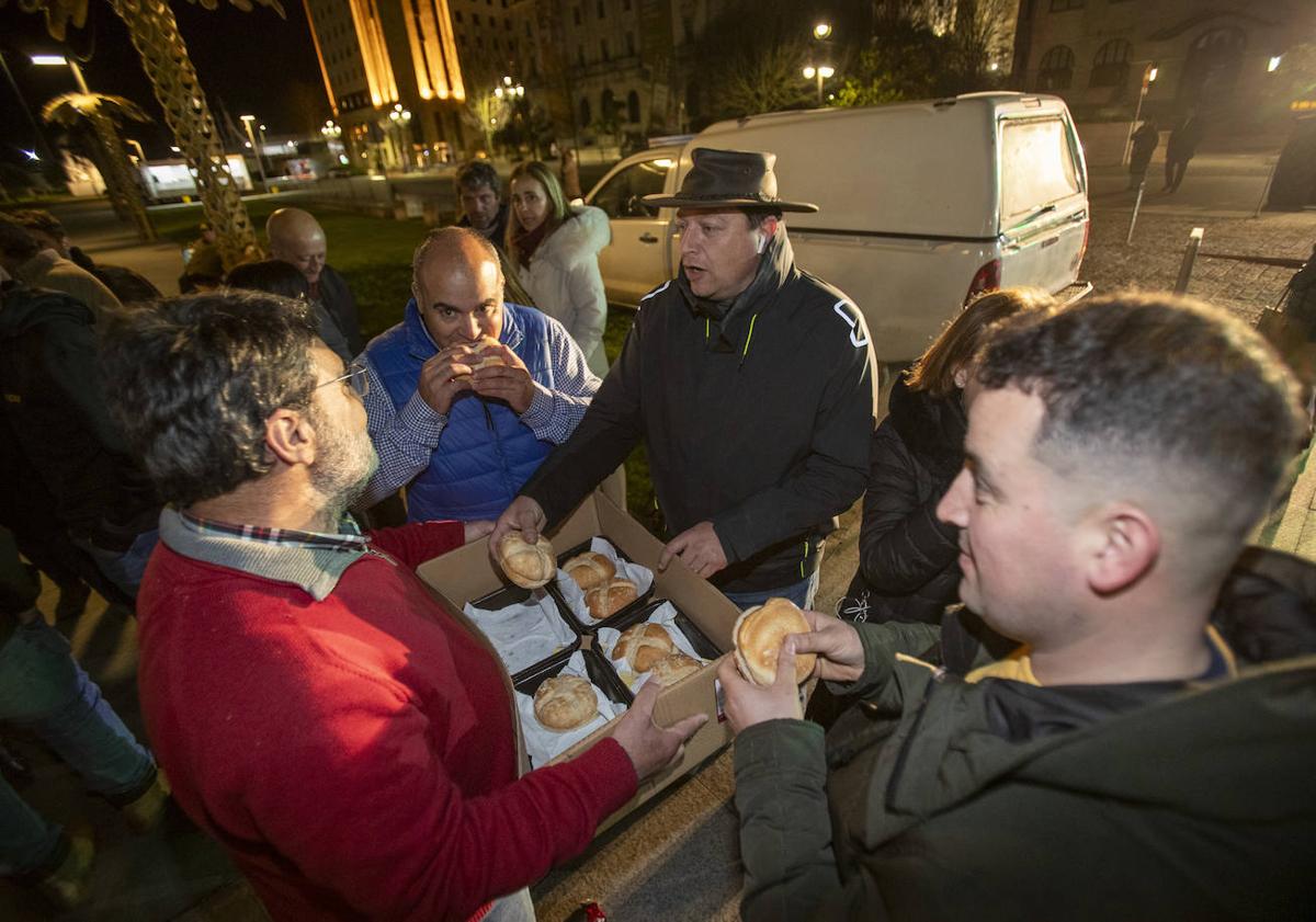 Imagen principal - Los responsables de la protesta reparten bocadillos a los ganaderos que hicieron noche en Santander. A la izquierda, los tractores pernoctaron en un carril de la calle Calvo Sotelo. Y, a la derecha, la exdiputada Marta García corta jamón junto a una compañera para acompañar la cena