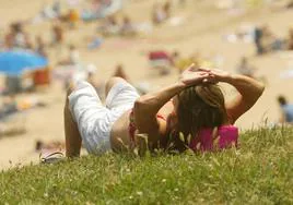 Una joven disfruta de sol tumbada sobre la hierba, frente a a playa, en Santander.