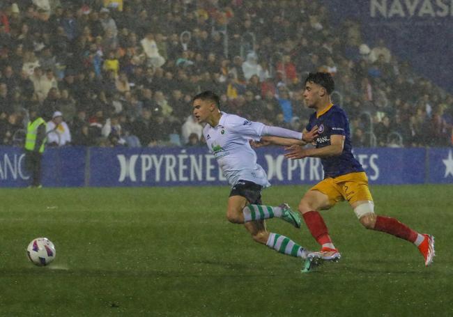 Mario García intenta llegar al balón antes que el rival bajo una intensa lluvia.