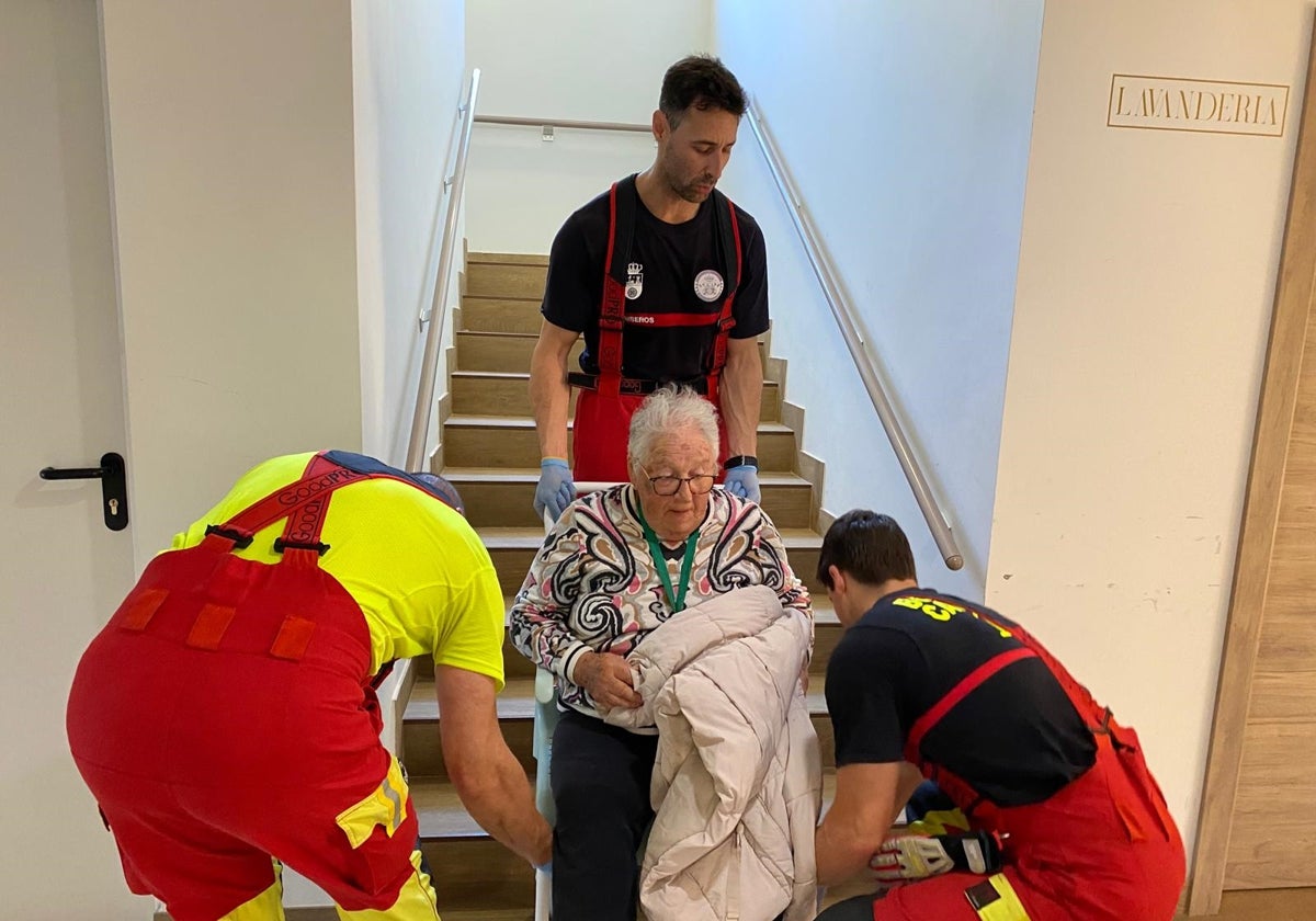 Bomberos del 112 de Tama suben por las escaleras a una anciana de la residencia de Aliezo