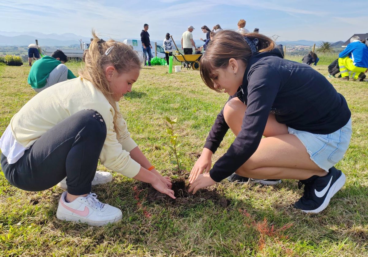 Dos alumnas del colegio Costa Quebrada plantan una encina en una parcela, en la sierra de Soto de la Marina.