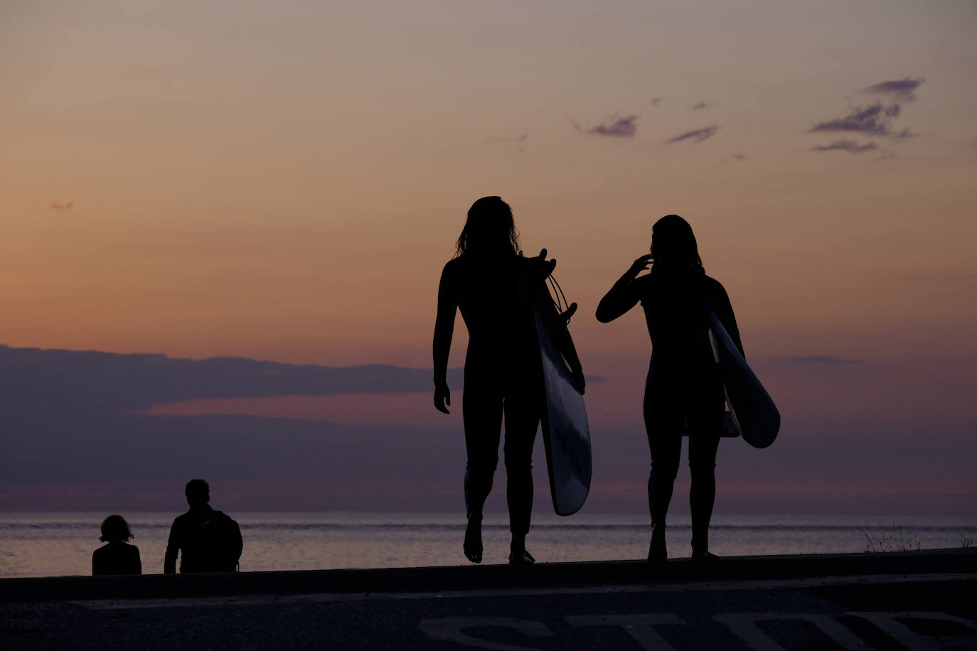 Surfistas van al agua a la hora del atardecer, en la playa de Oyambre.