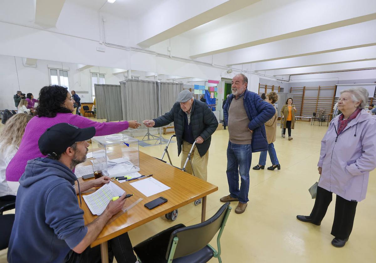 Un hombre entrega su carné de identidad a la presidenta de la mesa electoral antes de votar en el IES Marqués de Santillana de Torrelavega.