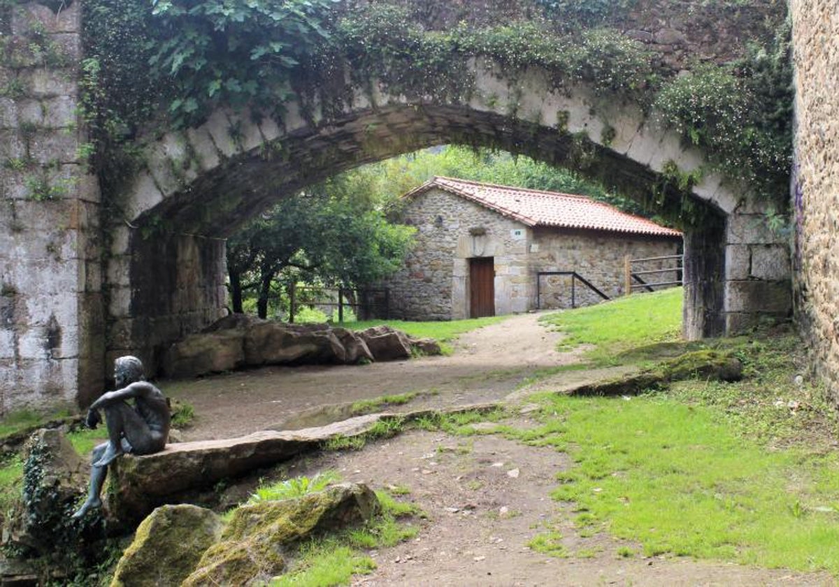 Escultura que recrea al protagonista de la leyenda situada junto al puente medieval con el edificio del museo al fondo.