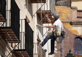 Un pintor arregla una fachada colgado con un arnés.