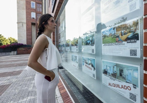 Una joven contempla el escaparate de ofertas de una inmobiliaria de Bezana