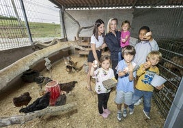 Carolina Crespo enseña el gallinero a una clienta y varios niños muestran el huevo que acaban de recoger.