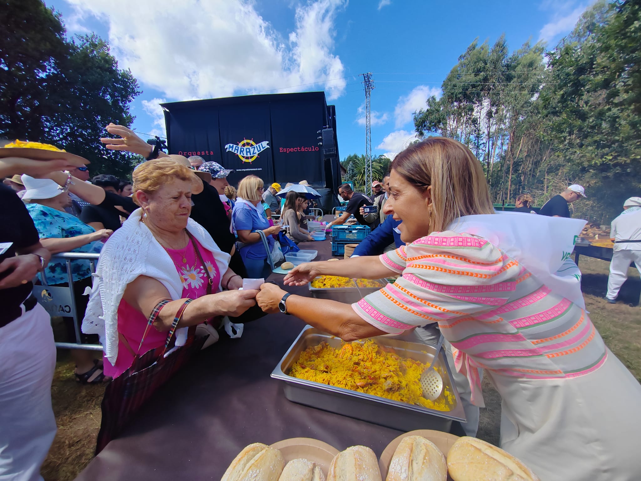 La presidenta regional no dudó en ayudar a los voluntarios a repartir las raciones de paella en día de la patrona de Piélagos