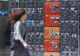 Una mujer pasea ante un escaparate con anuncios de pisos.