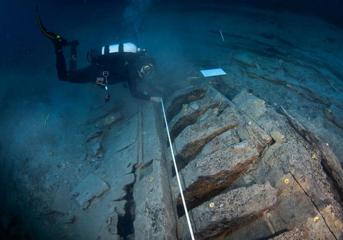 Arqueólogo subacuático inspeccionando un pecio. A la derecha, un dibujo de dos galeones del siglo XVII.