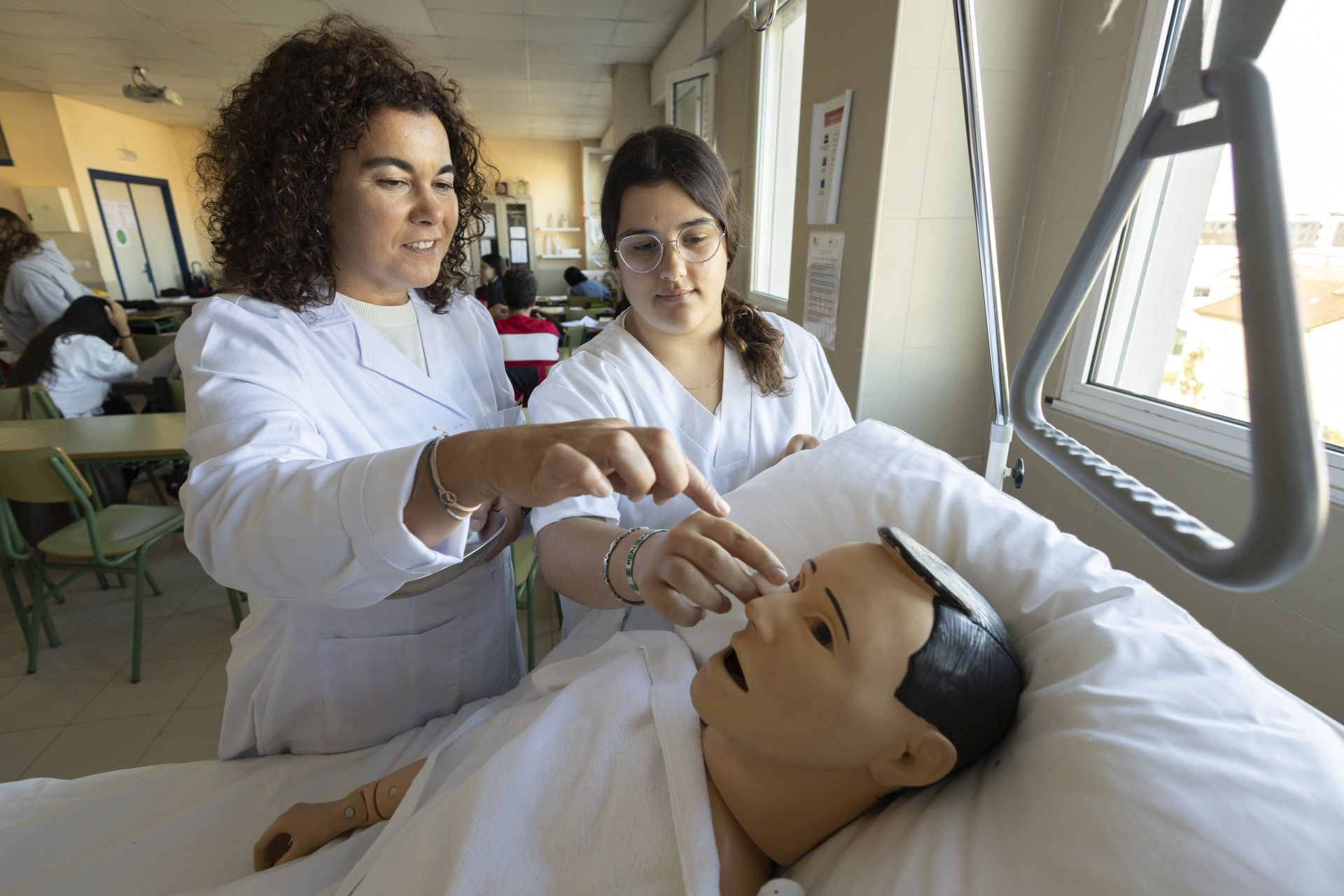 La profesora Emma Pena Alonso y la alumna Alba Bielsa realizan una práctica de "higiene de cara del paciente" en el aula del grado medio de Cuidados Auxiliares de Enfermería del IES Cantabria (Santander). aciente