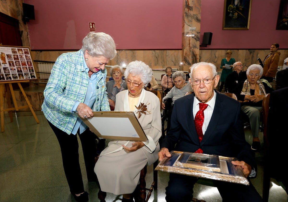 La presidenta de la Fundación, Mercedes Izárraga, entrega la placa a una de las vecinas homenajeadas en el acto, este miércoles, en el salón de actos del Asilo de Torrelavega.