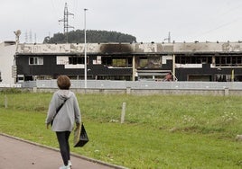 Una vecina camina por el Bulevar Ronda, con el bazar de la cadena Siglo calcinado al fondo, en Campuzano (Torrelavega).