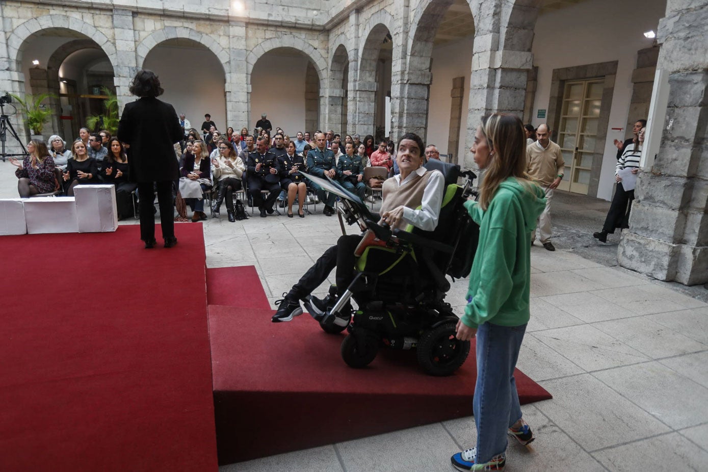 Una persona con discapacidad sube por la rampa al escenario para participar en el acto.