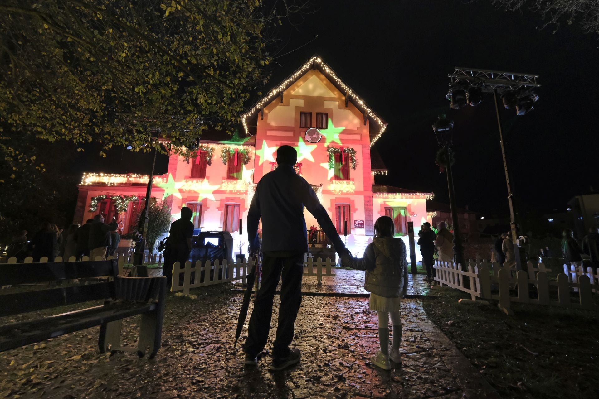 Un padre y su hija de la mano frente a la casa de la Navidad.