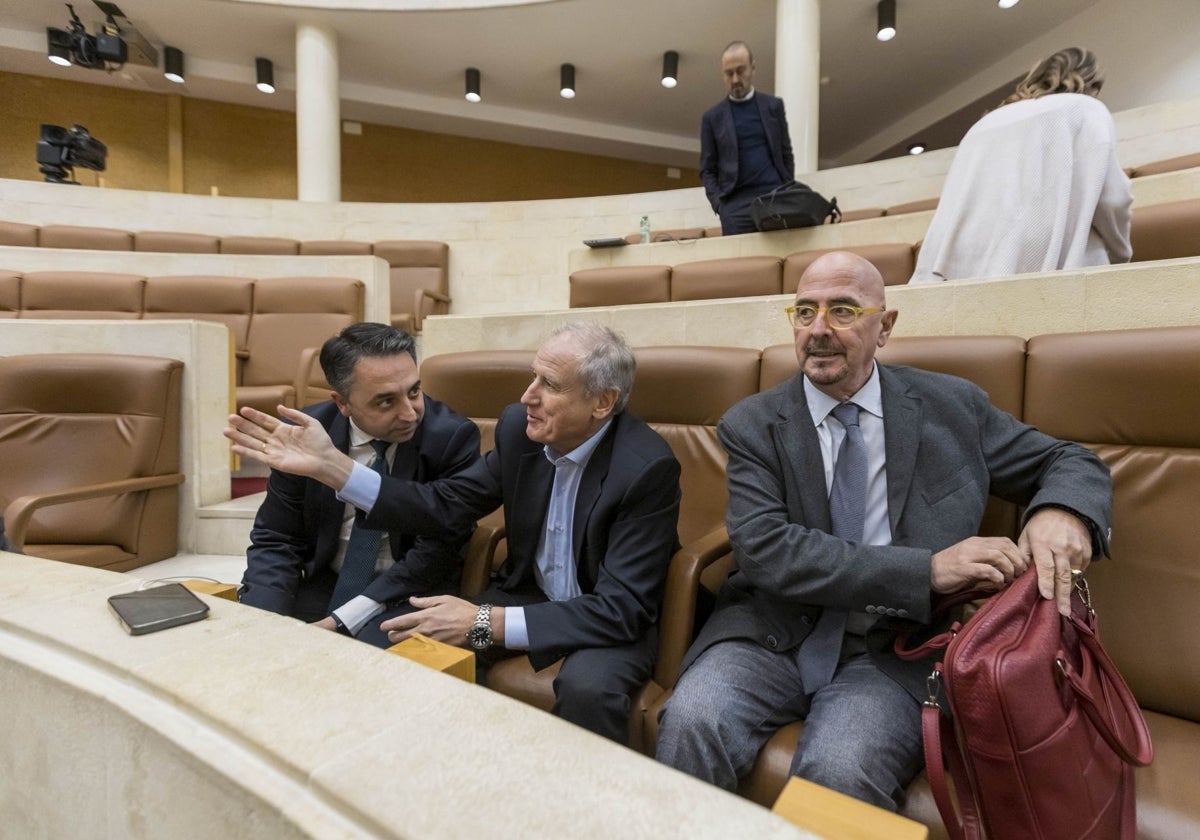 El consejero de Salud, César Pascual, abre su mochila mientras Carlos Caramés y Eduardo Arasti charlan a su lado.