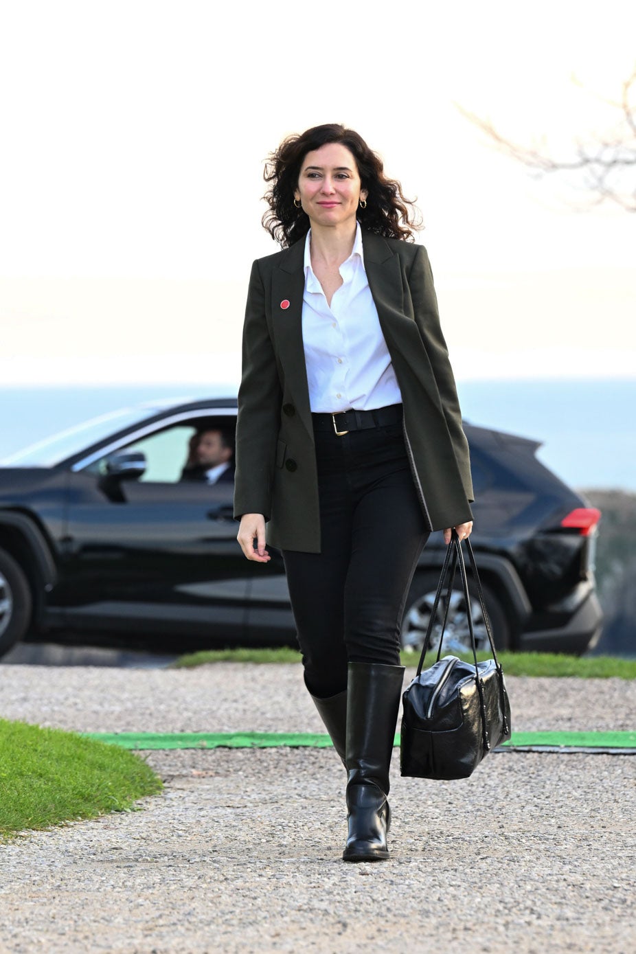 Isabel Díaz Ayuso, la presidenta de la Comunidad de Madrid, eligió un pantalón negro, camisa blanca y americana verde oscuro, que completó con unas botas negras planas hasta las rodillas y un gran bolso del mismo color. 