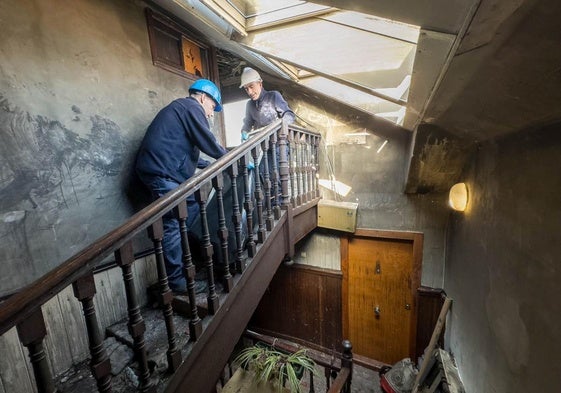 Dos trabajadores de una empresa de limpieza, ayer, despejan el acceso al ático en el que vivían las dos víctimas mortales del incendio de la calle Juan de la Cosa, en Santander.