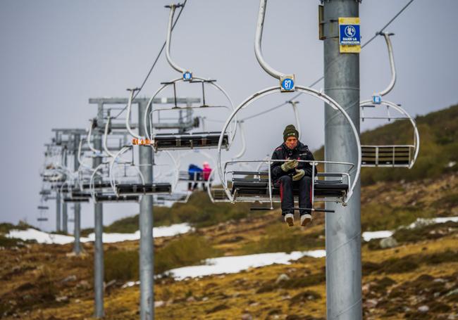 Un esquiador en un telesilla en Alto Campoo, con escasa nieve en la estación.