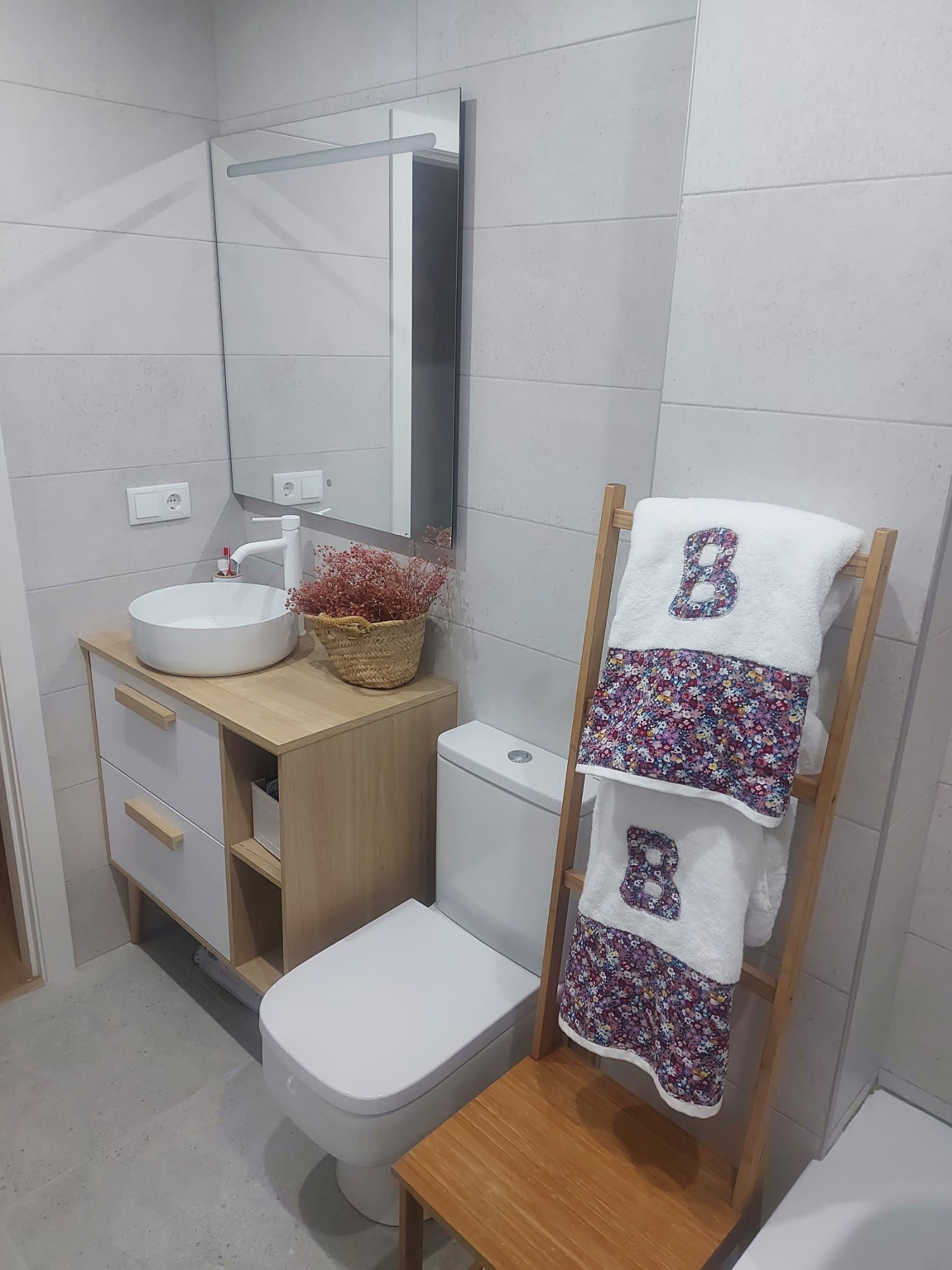 Este baño combina funcionalidad y calidez con mueble y toallero de madera y toallas personalizadas.