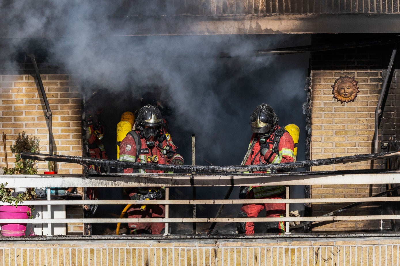 Efectivos del parque de bomberos de Torrelavega trabajan juntos en el foco del incendio, frente a un denso humo negro procedente de la vivienda afectada.