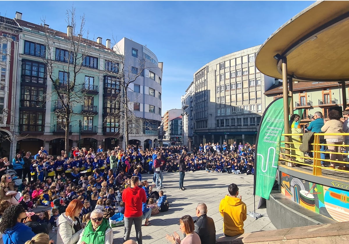 Alumnos atienden sentados en la Plaza Mayor, durante la entrega del cheque en el quiosco, a la Asociación Española Contra el Cáncer.