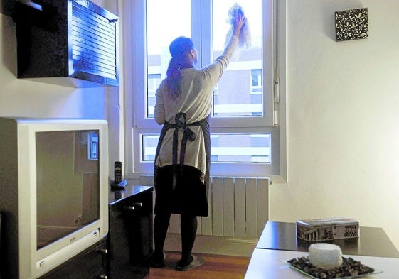 Una mujer empleada en el servicio doméstico limpia una ventana en la vivienda de una familia española.