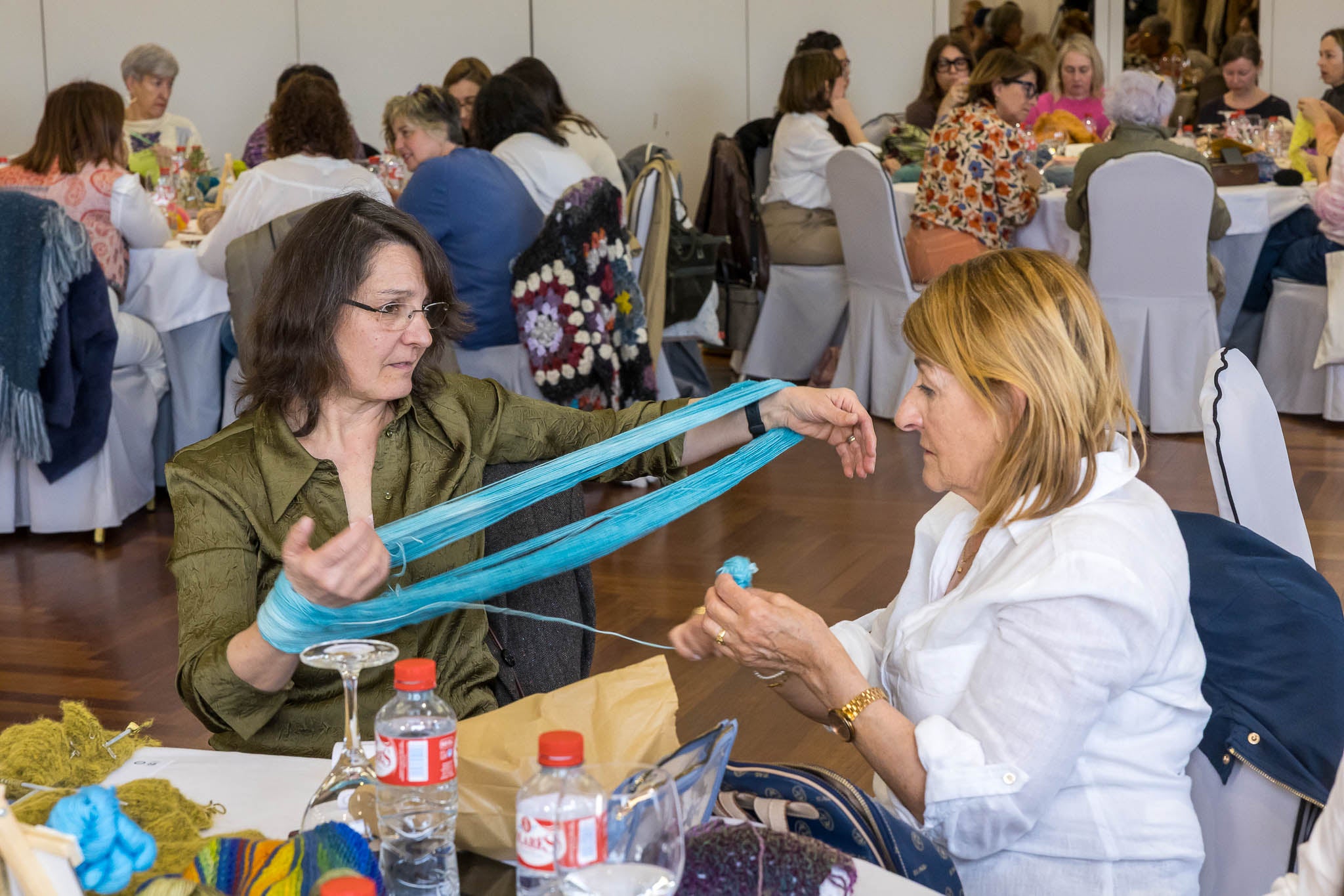 Dos mujeres se ayudan a recoger un ovillo de lana.