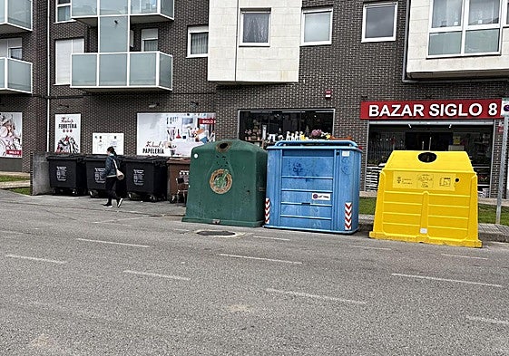 Una mujer pasa por delante de un grupo de contenedores en una calle de Renedo de Piélagos.