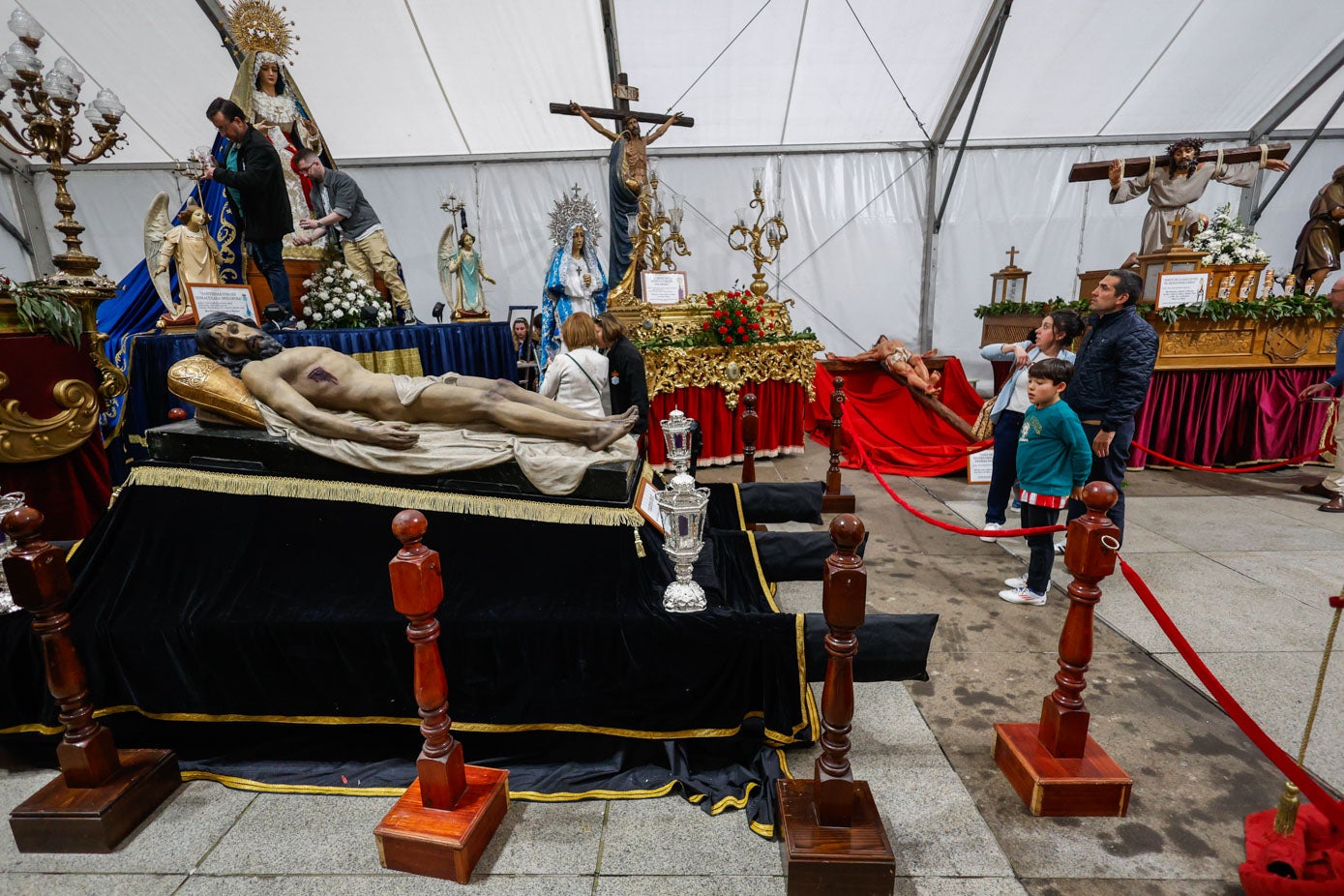 Tres personas observan el Cristo Yacente, mientras otras dos trabajan en el adorno la Dolorosa.