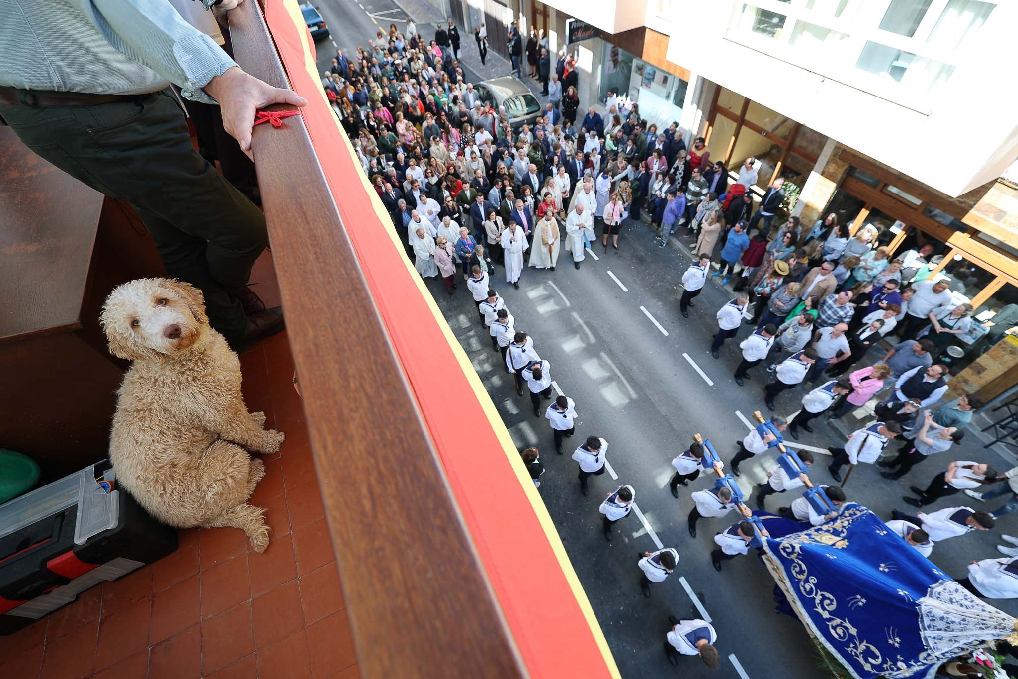 Un perro junto a su dueño siguiendo la procesión desde el balcón