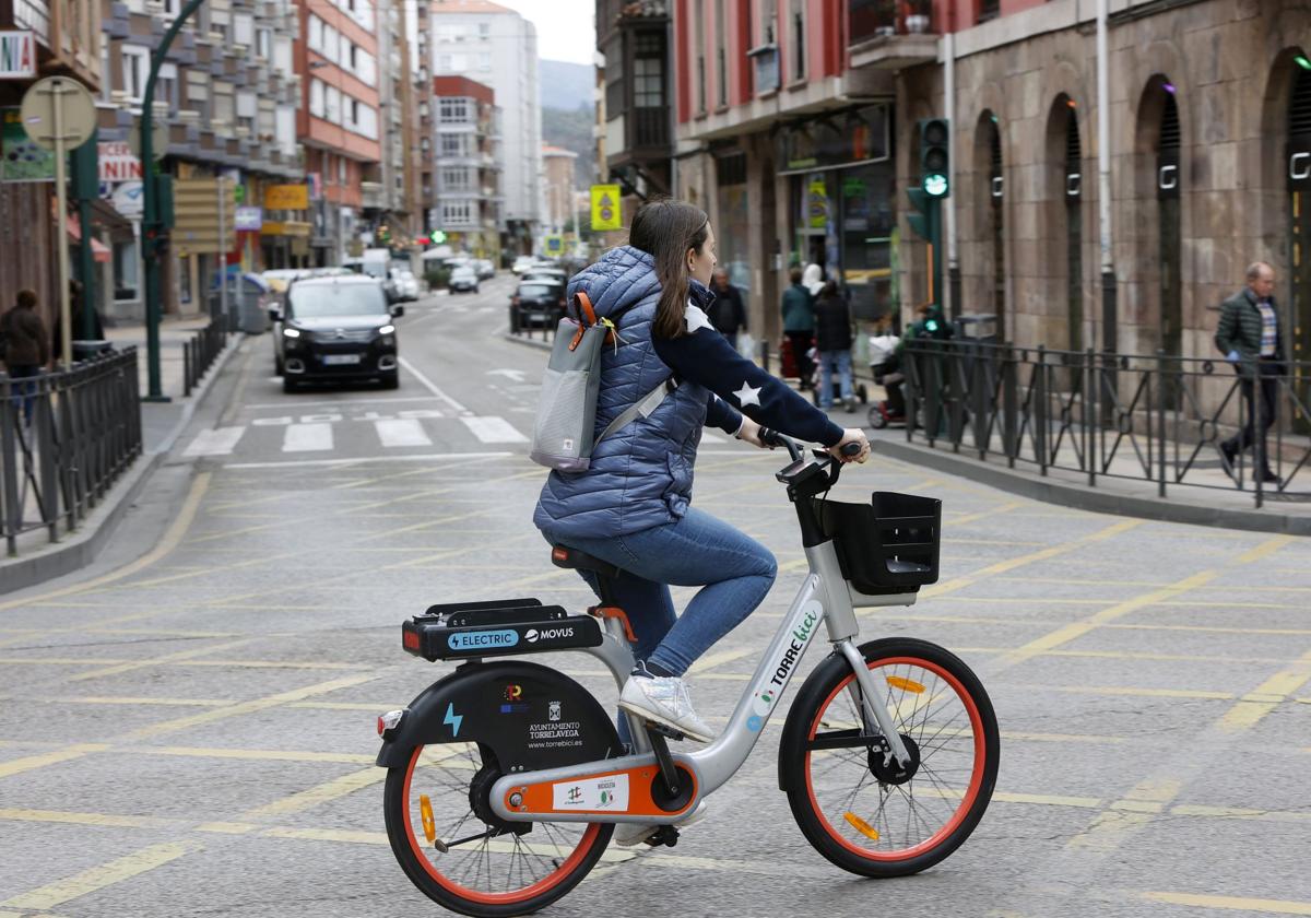 Una vecina circula con una bicicleta eléctrica de Torrelavega, en el cruce de Cuatro Caminos.