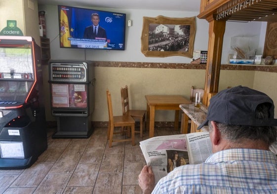 Un vecino de la zona ojea el perfil de Leire Díez en el periódico mientras Núñez Feijóo denuncia el caso en televisión.