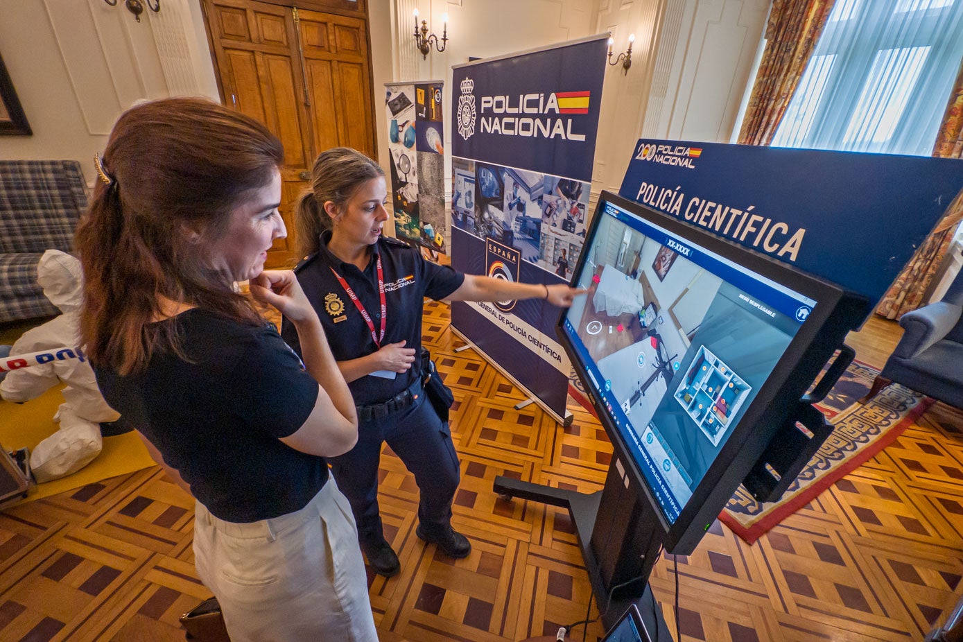 Una agente señala el panel instalado con motivo del encuentro de la Policía Nacional en la UIMP.