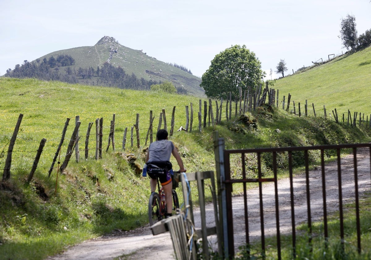 Un ciclista circula por la sierra del Dobra; al fondo, el pico de la Capía.