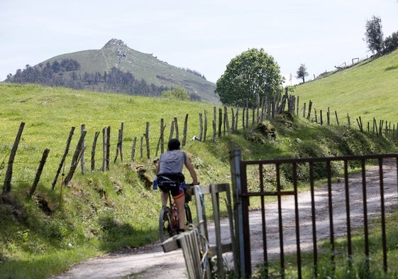 Un ciclista circula por la sierra del Dobra; al fondo, el pico de la Capía.
