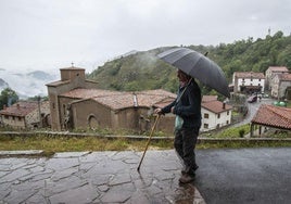 Un vecino de Tresviso pasea bajo la lluvia por una calle de la localidad.