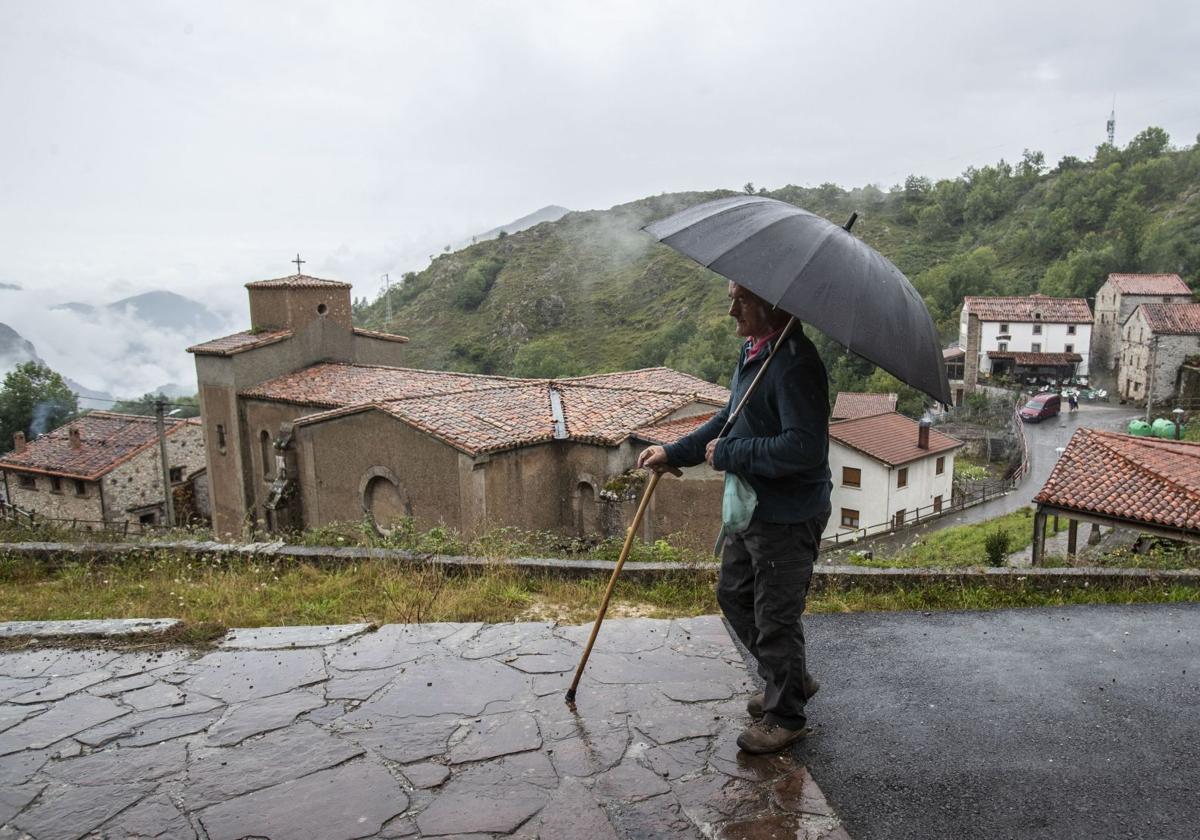 Un vecino de Tresviso pasea bajo la lluvia por una calle de la localidad.