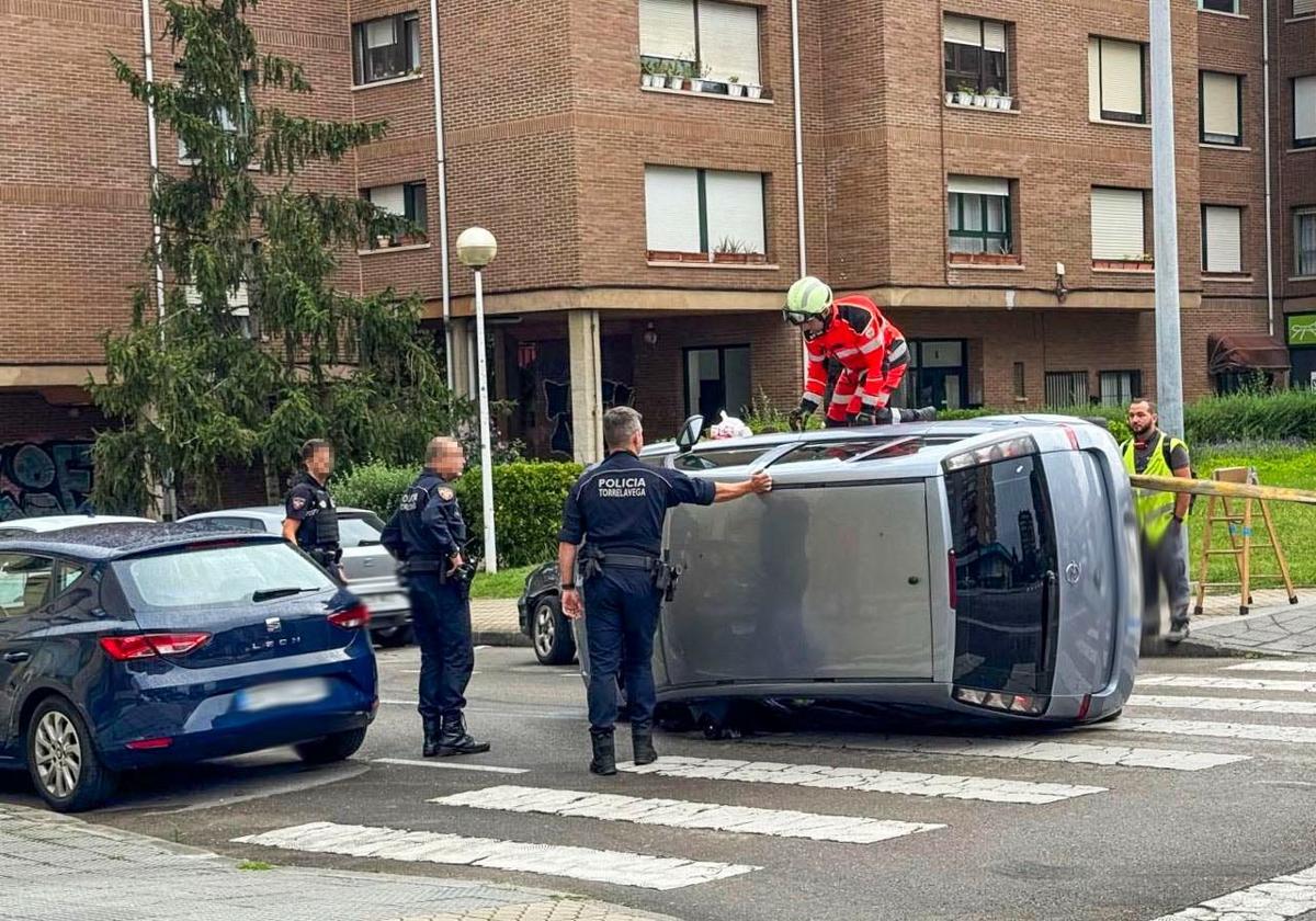Policías y bomberos intervienen para rescatar a la conductora del vehículo volcado, este martes, en El Zapatón (Torrelavega).