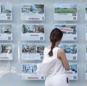 Una mujer mira anuncios de venta de viviendas en el escaparate de una agencia inmobiliaria.