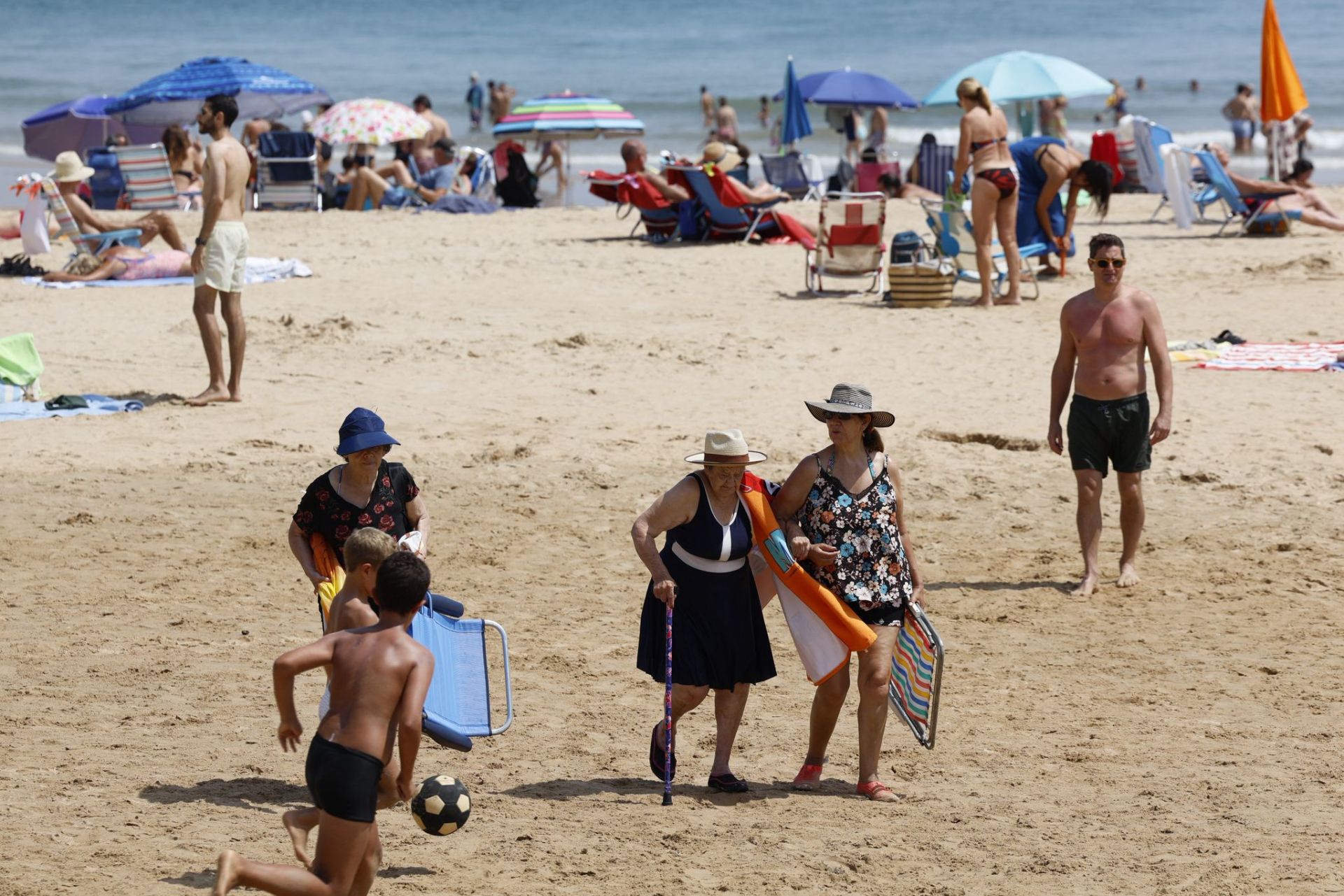 Niños jugando al fútbol y mujeres en busca de un lugar donde colocar la silla para disfrutar de un día de playa