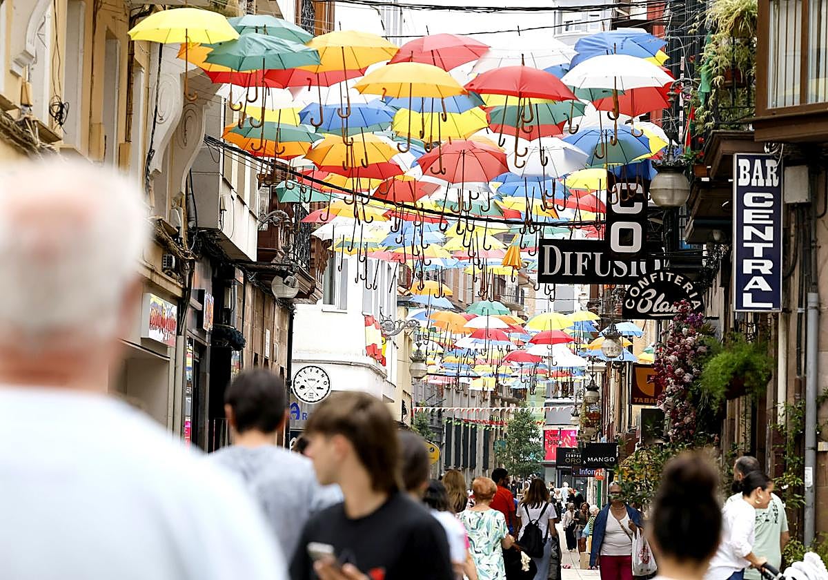 Vecinos caminan por la calle Consolación de Torrelavega, decorada con decenas de paraguas durante las fiestas.