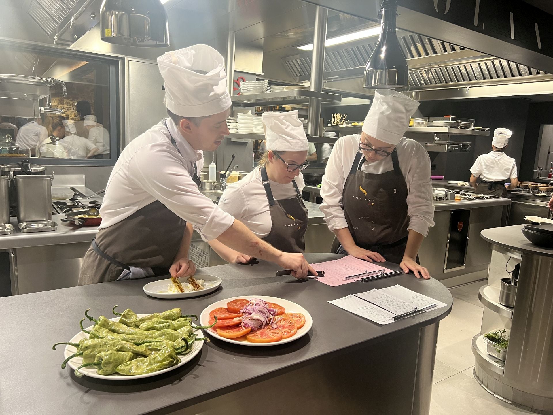 Las comandas comienzan a acumularse en la mesa de pase y Lucas, Cristina y Alejandra se reparten cometidos mientras algunos platos están esperando a que lleguen los camareros para que se los lleven al bar.