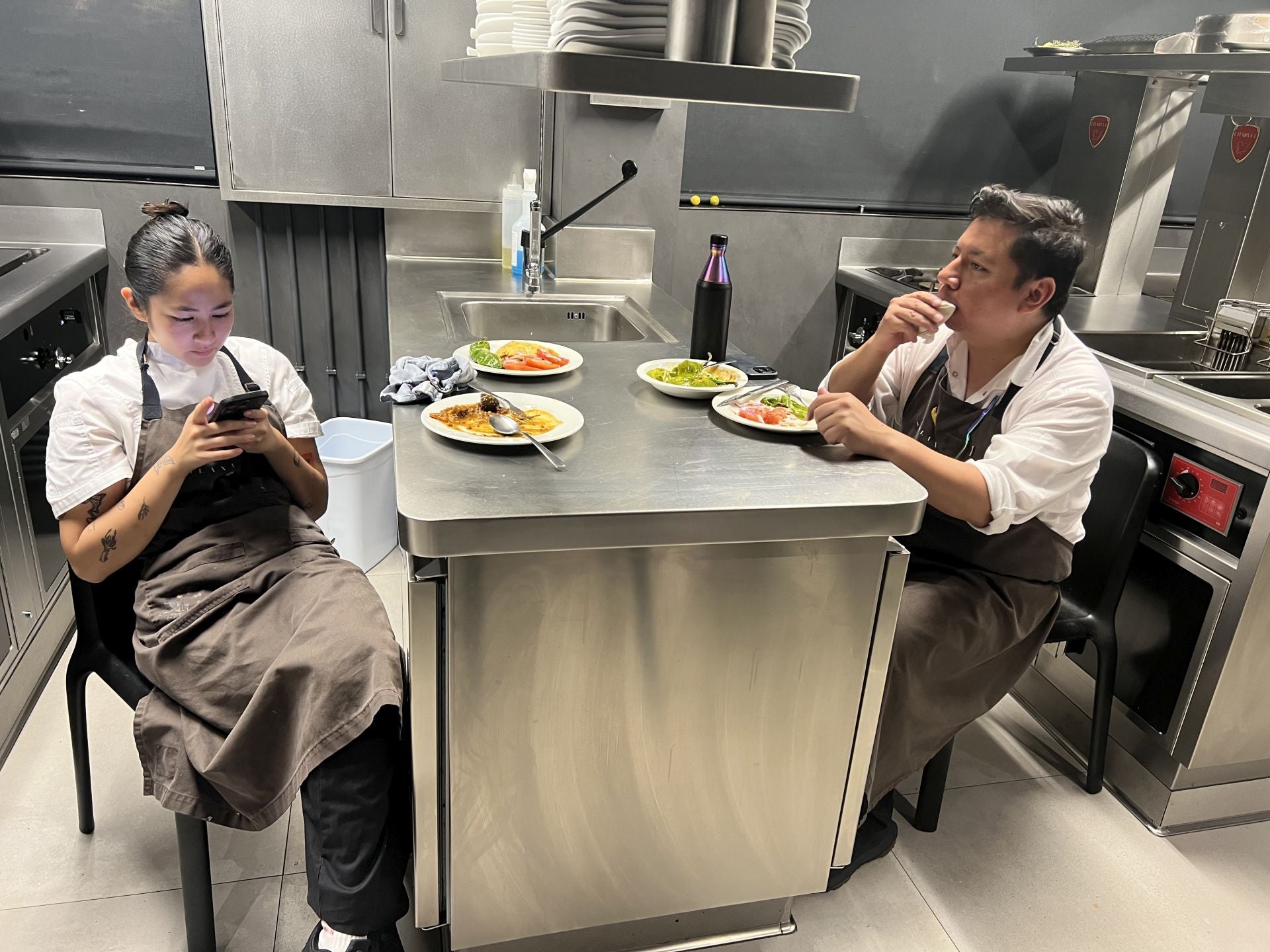 En torno a las 17.30 horas, después de haber concluido el servicio de comidas y de haber limpiado a fondo toda la cocina, los miembros del equipo, a medida que concluyen sus tareas, comen en la propia cocina. Hoy toca una ensalada de tomate, un guiso de lentejas, pimientos verdes y algo de la última tortilla que se elaboró por la mañana. En la foto, Ana consulta su teléfono y Fernando da cuenta de la ensalada.