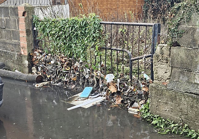 Residuos que traen las fuertes lluvias acumulados en una reja en frente del garaje comunitario.