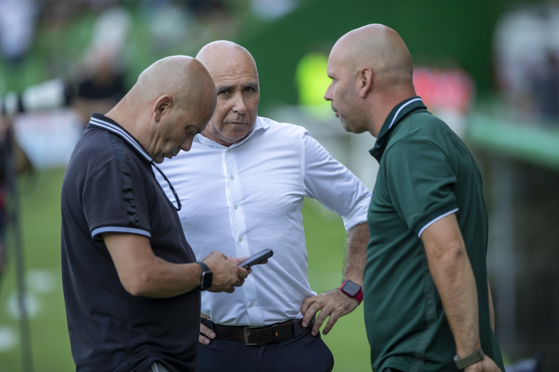 Chema Aragón ojea su móvil mientras conversa con Manolo Higuera y José Alberto López en los Campos de Sport.