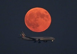 Un avión sobrevuela el cielo, con la luna roja de fondo.