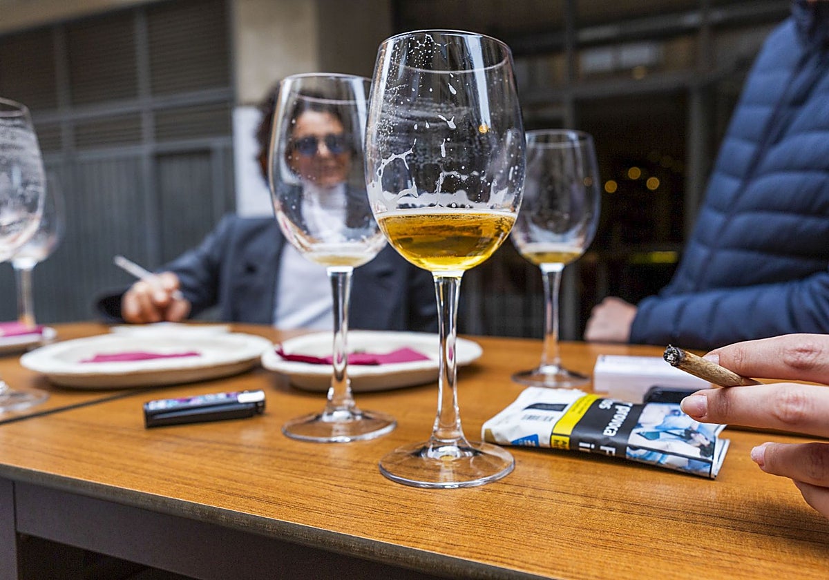 Unos clientes toman unas cañas y fuman en la terraza de un bar.